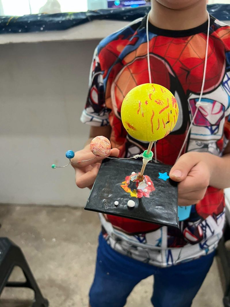 Un niño muestra el sistema solar que armó en el taller: un Sol amarillo y planetas de colores sobre una base negra.